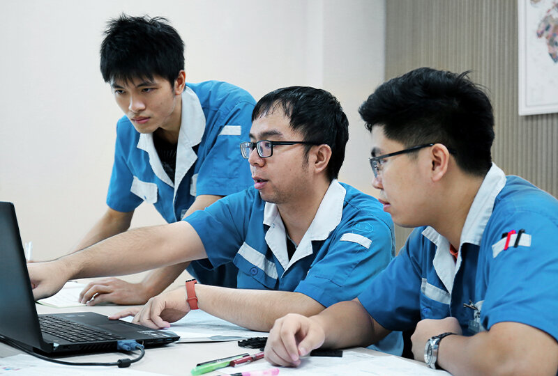 3 chinesische Ingenieure in vor einem Laptop diskutieren eine technische Zeichnung