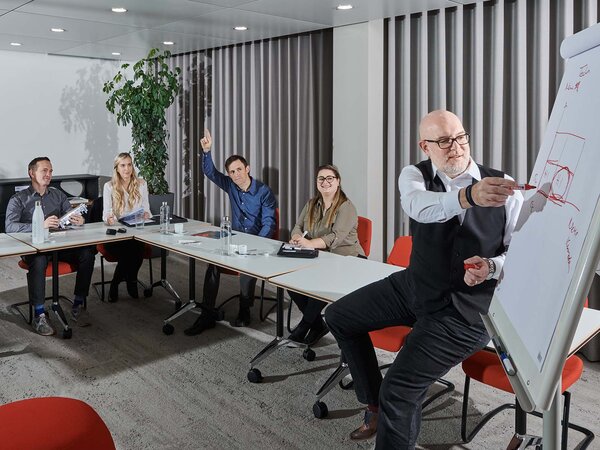 man presents and points to the flipchart with red pen while four employees actively participate in the course