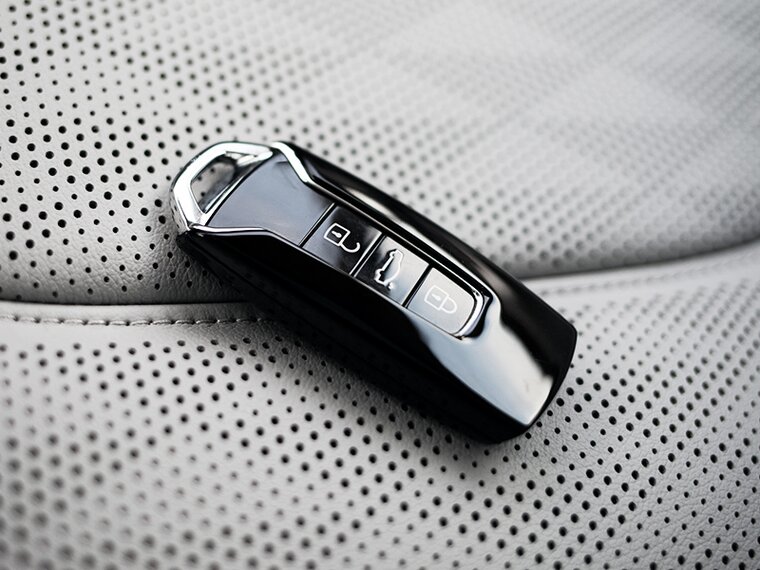 Detailaufnahme von glänzendem schwarzen Autoschlüssel auf perforiertem hellgrauen Ledersitz