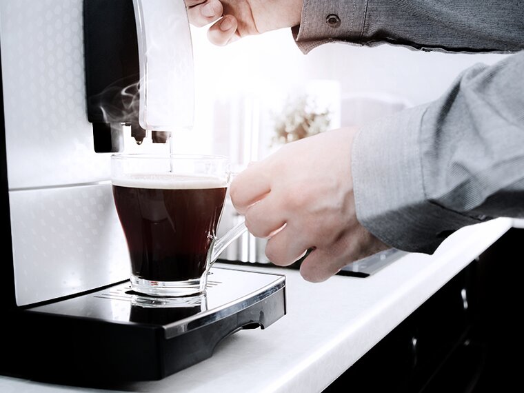 Weissware Detailaufnahme einer männlichen Hand mit Kaffeertasse an einem modernen Vollautomaten